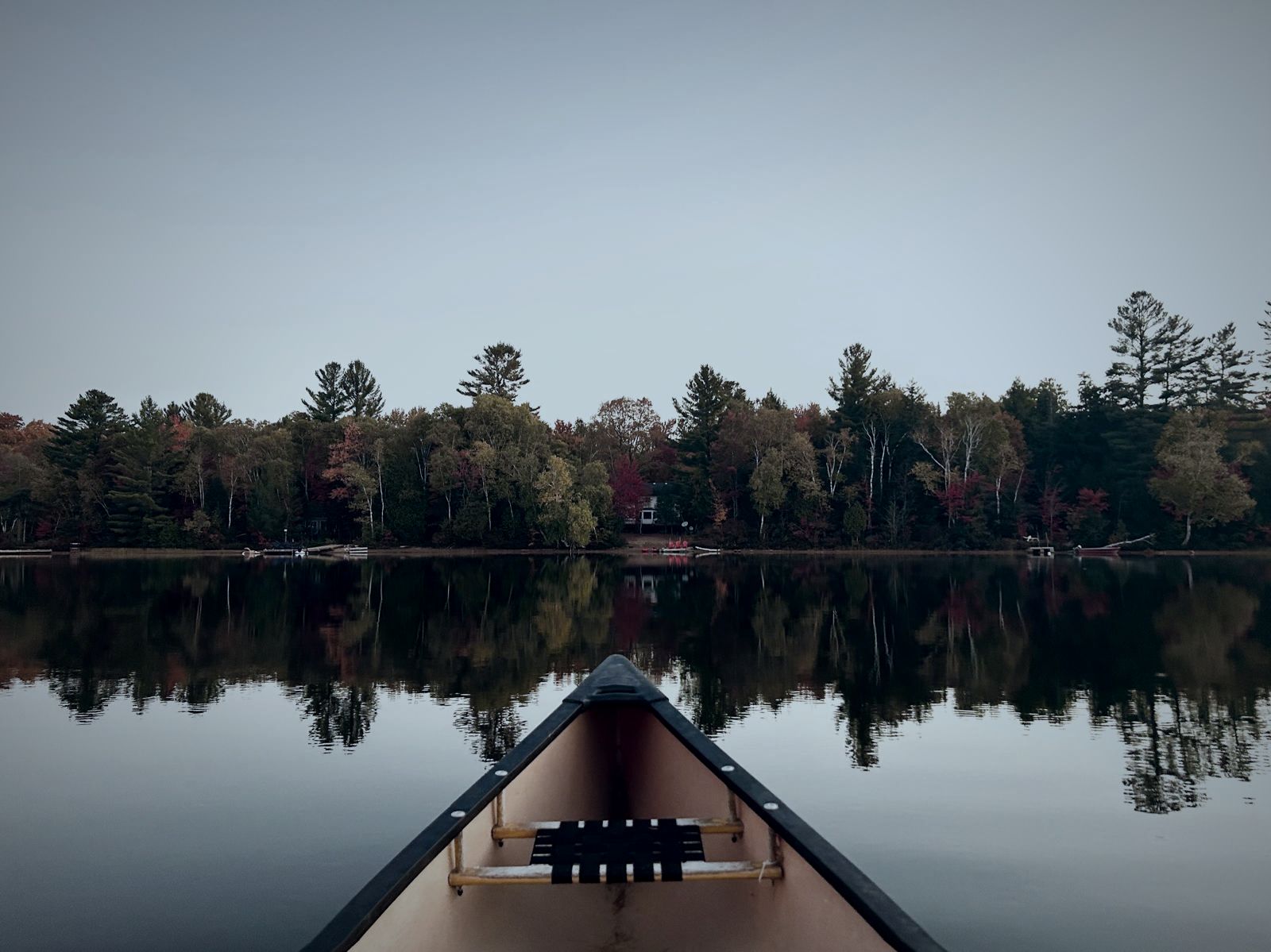 Bow of a canoe on a mirror-still lake lined with autumn trees